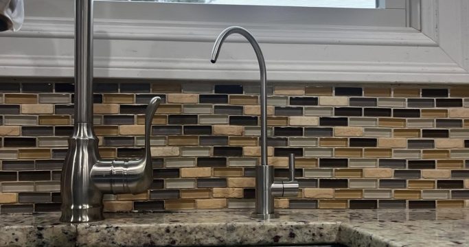 Plumber repairing leaking kitchen sink pipe in Long Island house
